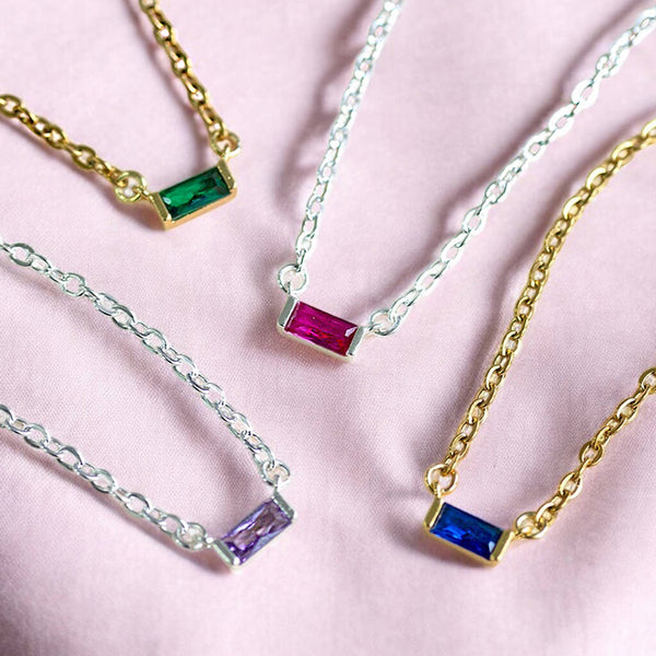 Colourful baguette birthstone necklaces in gold and silver tones, featuring green, pink, purple and blue stones.
