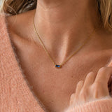 Dainty gold-tone baguette birthstone necklace with a vivid blue stone, styled simply for an everyday pop of colour.