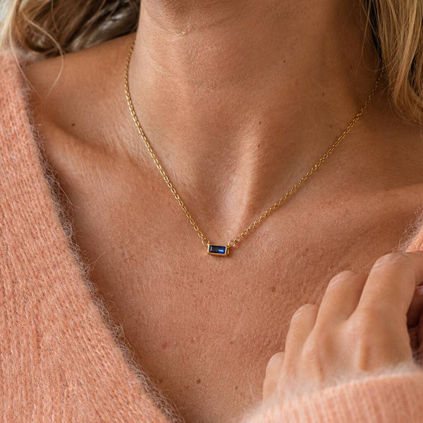 Dainty gold-tone baguette birthstone necklace with a vivid blue stone, styled simply for an everyday pop of colour.