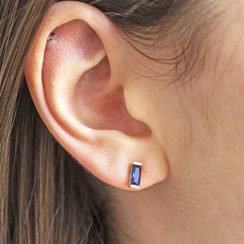 Silver dainty baguette birthstone stud earrings shown in Sapphire September birthstone worn on an ear.