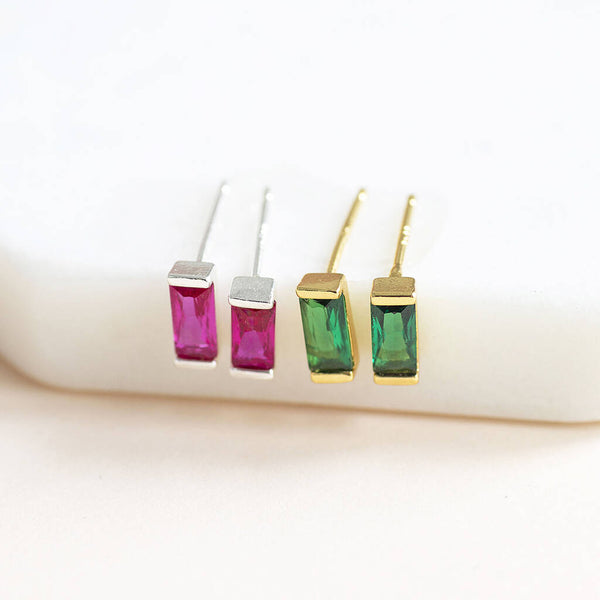 Two pairs of dainty baguette birthstone stud earrings one in silver July birthstone and one in gold Emerald birthstone.