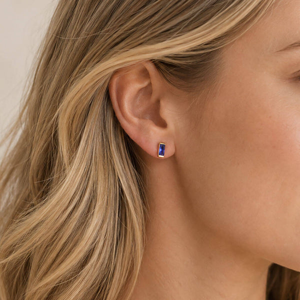 Dainty blue baguette birthstone stud in a gold-tone setting, adding a sleek pop of colour to an everyday ear stack.