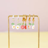 Image shows from left too right, silver plated white Daisy Huggie Hoop Earrings, gold plated pale pink Daisy Huggie Hoop Earrings, gold plated dark pink Daisy Huggie Hoop Earrings and gold plated white Daisy Huggie Hoop Earrings.