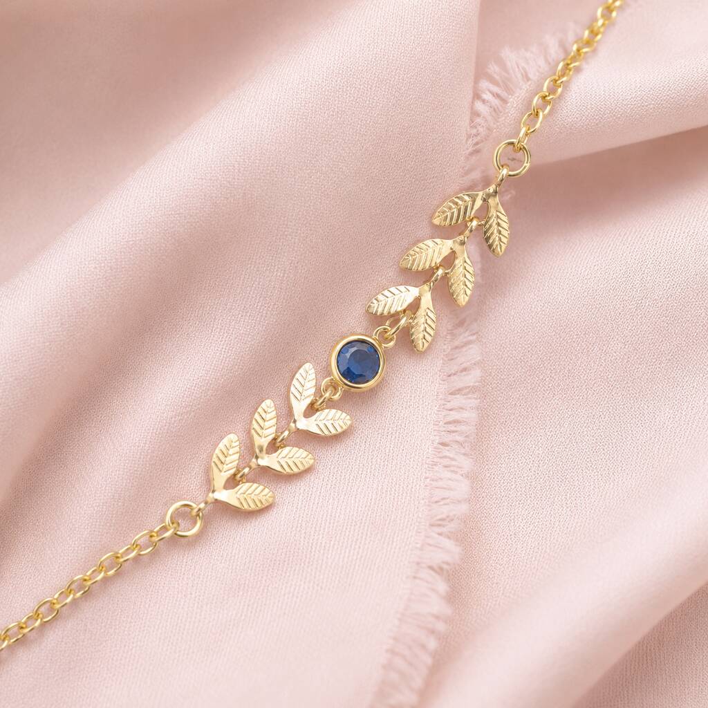 Close-up of a gold plated vine bracelet with sapphire blue birthstone crystal on a soft pink fabric background
