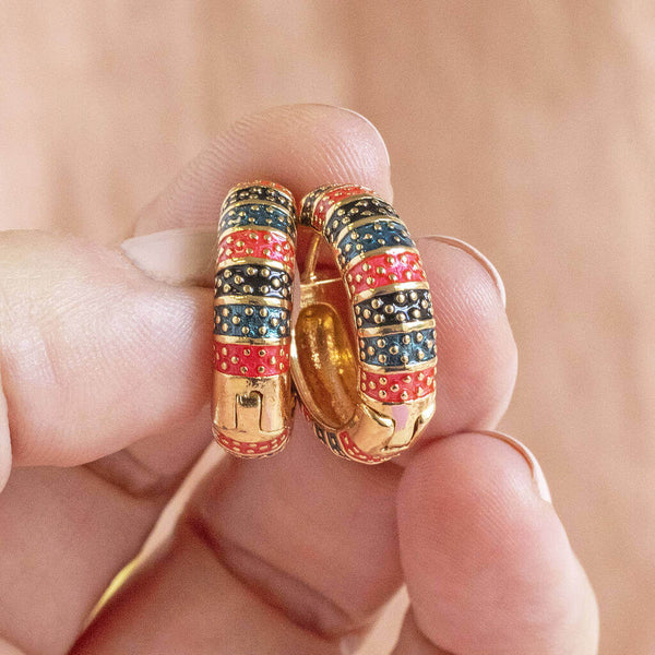 Model holds Dotted Stripey Enamel Huggie Hoop Earrings.