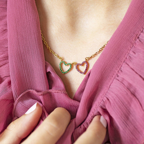 Image shows gold double birthstone heart necklace worn with a pink frill top.