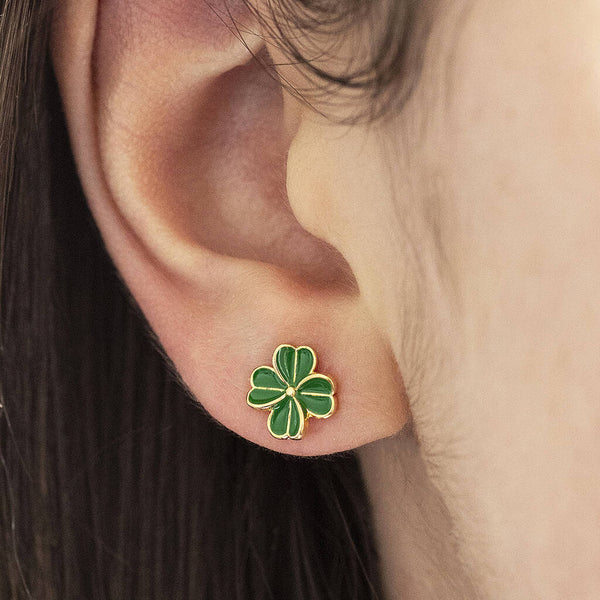 Gold enamel four leaf clover stud earrings worn on the ear.