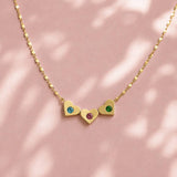 Gold heart necklace with blue, pink and green birthstone crystals, styled as a colourful everyday piece