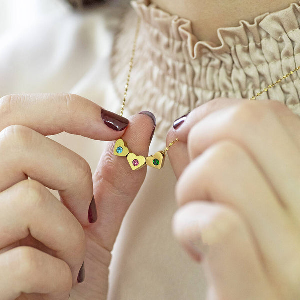 image shows a woman in a beige top wearing a giold necklace with family birthstone hearts