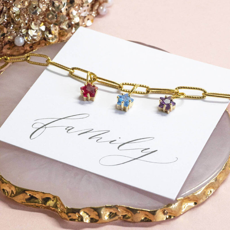 Image shows Gold Plated Family Birthstone Stars Bracelet with July, March and February birthstones. Bracelet is on a 'family' sentiment card on a pink backdrop.