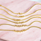 Gold flat chain bracelet displayed with various names made using gold initials in circular font