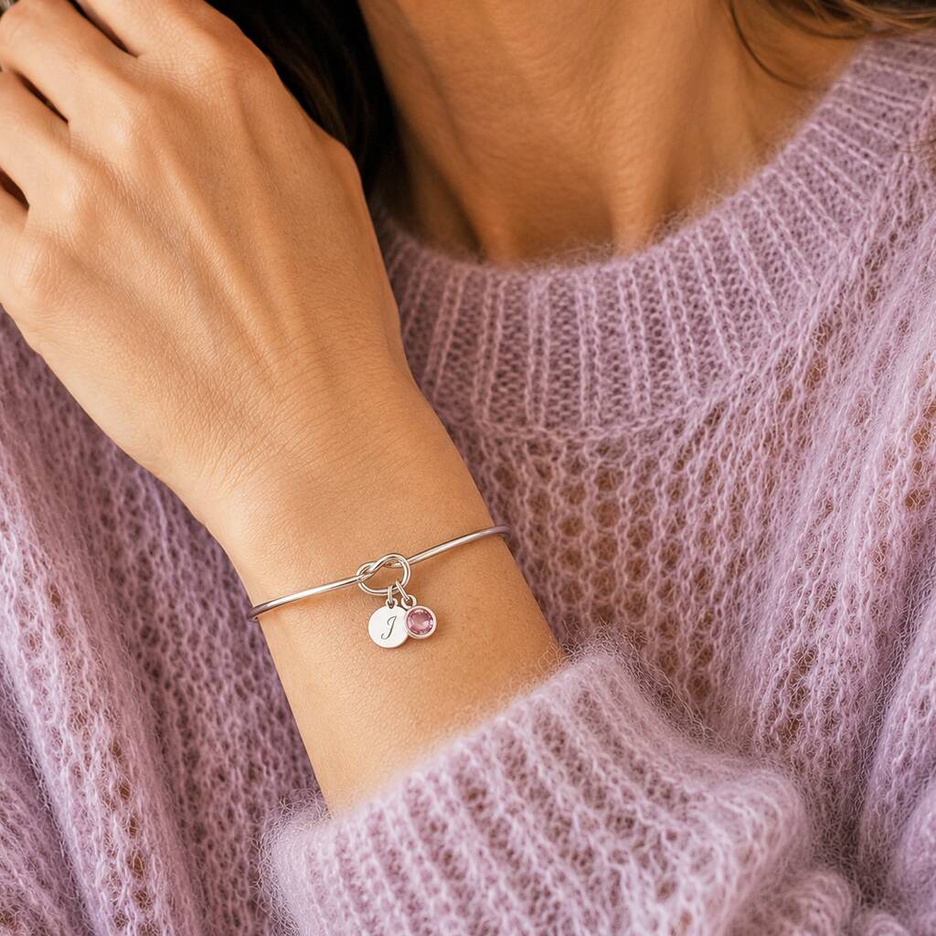 Silver knot bangle with pink crystal birthstone and initial charm, an elegant everyday accessory