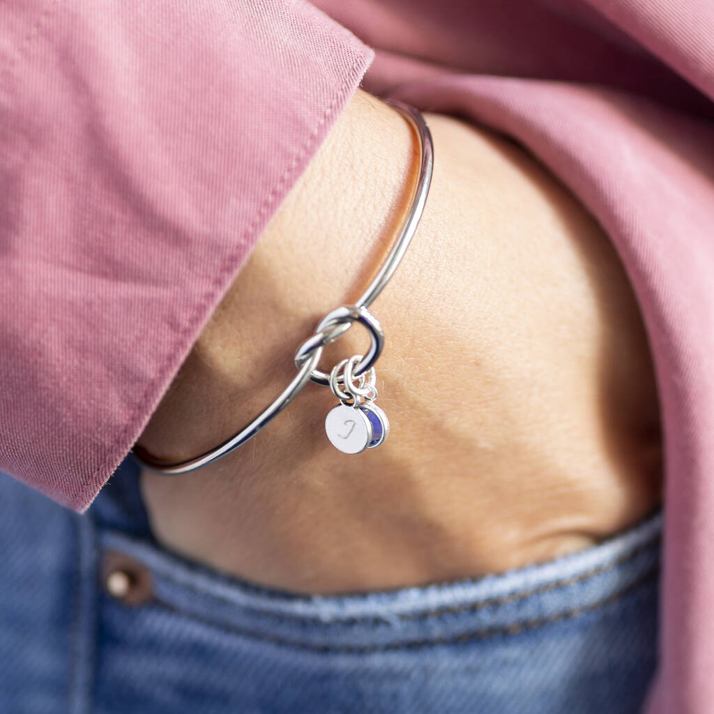 Silver friendship knot bangle featuring a blue crystal birthstone and initial charm for layering
