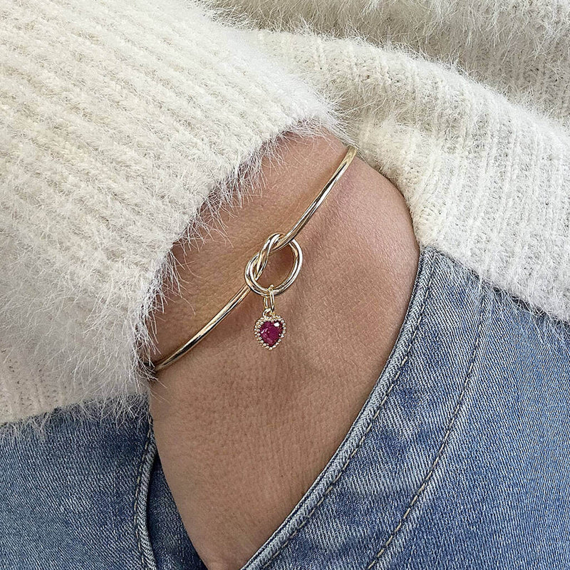 Image shows model wearing gold plated friendship knot bangle with a birthstone July Ruby heart.