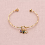 Gold plated friendship knot bangle with purple, green and clear heart birthstone charms on a soft pink backdrop