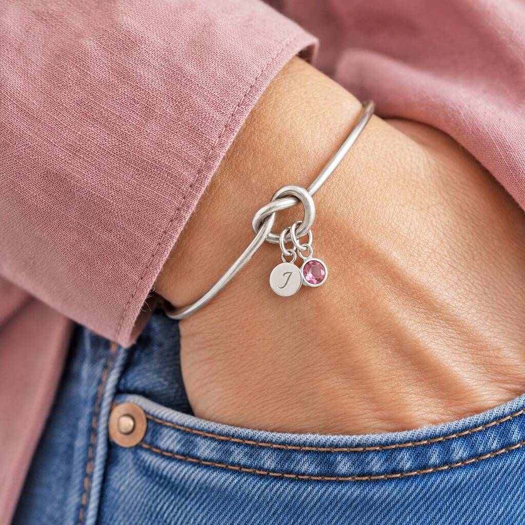 Silver friendship knot bangle with pink crystal birthstone and initial charm, perfect for stacking