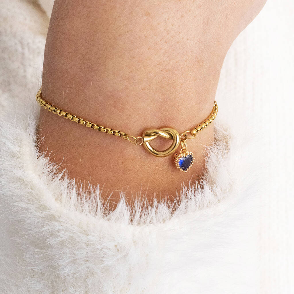 Image shows model in white fluffy jumper wearinga friendship knot bracelet with September Sapphire birthstone heart charm