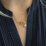 Image shows model in navy blue blouse wearing a friendship knot necklace with a clear crystal april birthstone heart