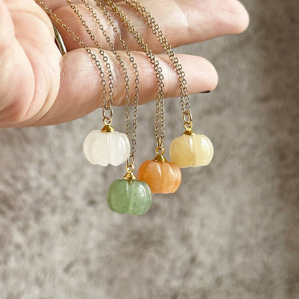 Image shows a hand holding four gemstone pumpkin necklaces on a gold plated chain