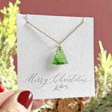 Image shows green glass Christmas tree charm suspended from a gold plated trace chain presented on a Merry Christmas sentiment card.