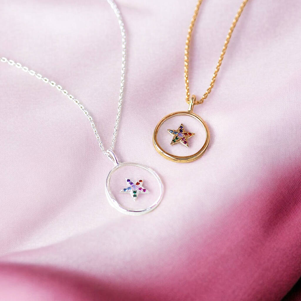 Image shows a silver and a gold crystal star glass pendants displayed on a piece of bright pink coloured material.