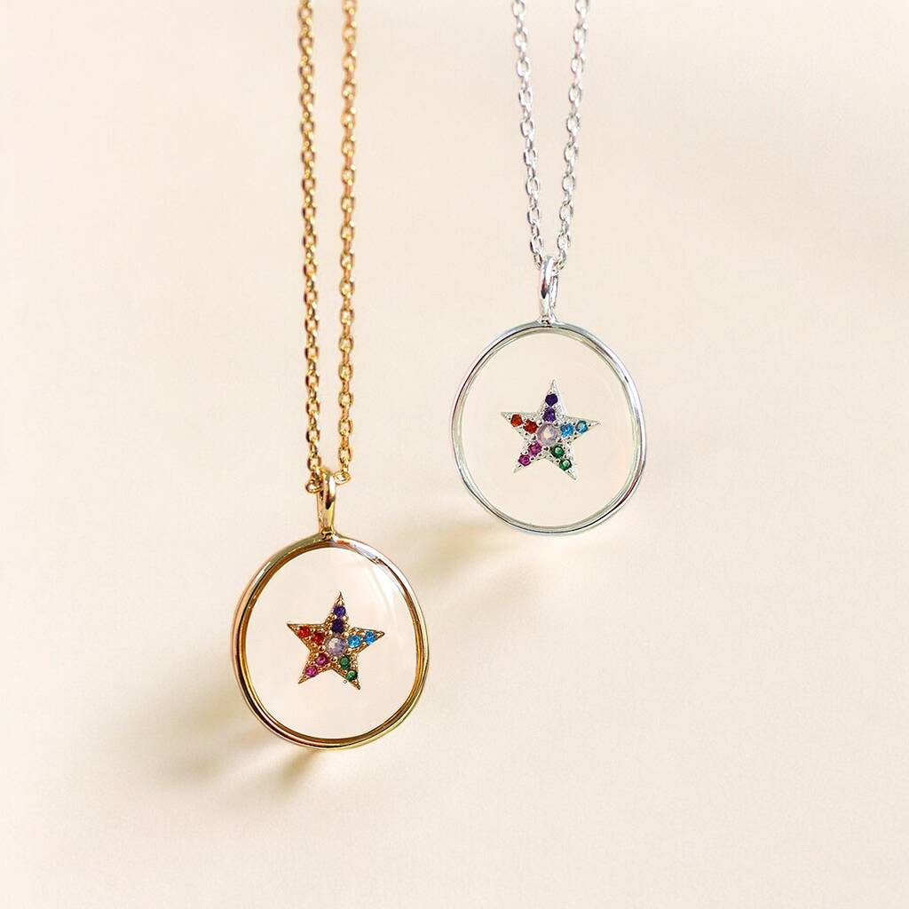 Image shows a silver and a gold crystal star glass pendants displayed on a piece of a neutral background.