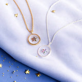 Image shows a silver and a gold crystal star glass pendants displayed on a piece of pastel coloured material.