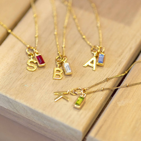Detail of rectangular baguette birthstone on gold necklace in various initials and birthstones