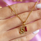 Close up of gold initial charm with baguette birthstone necklace