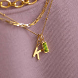 Layered gold plated initial necklace with green baguette birthstone charm, colourful personalised jewellery styling piece