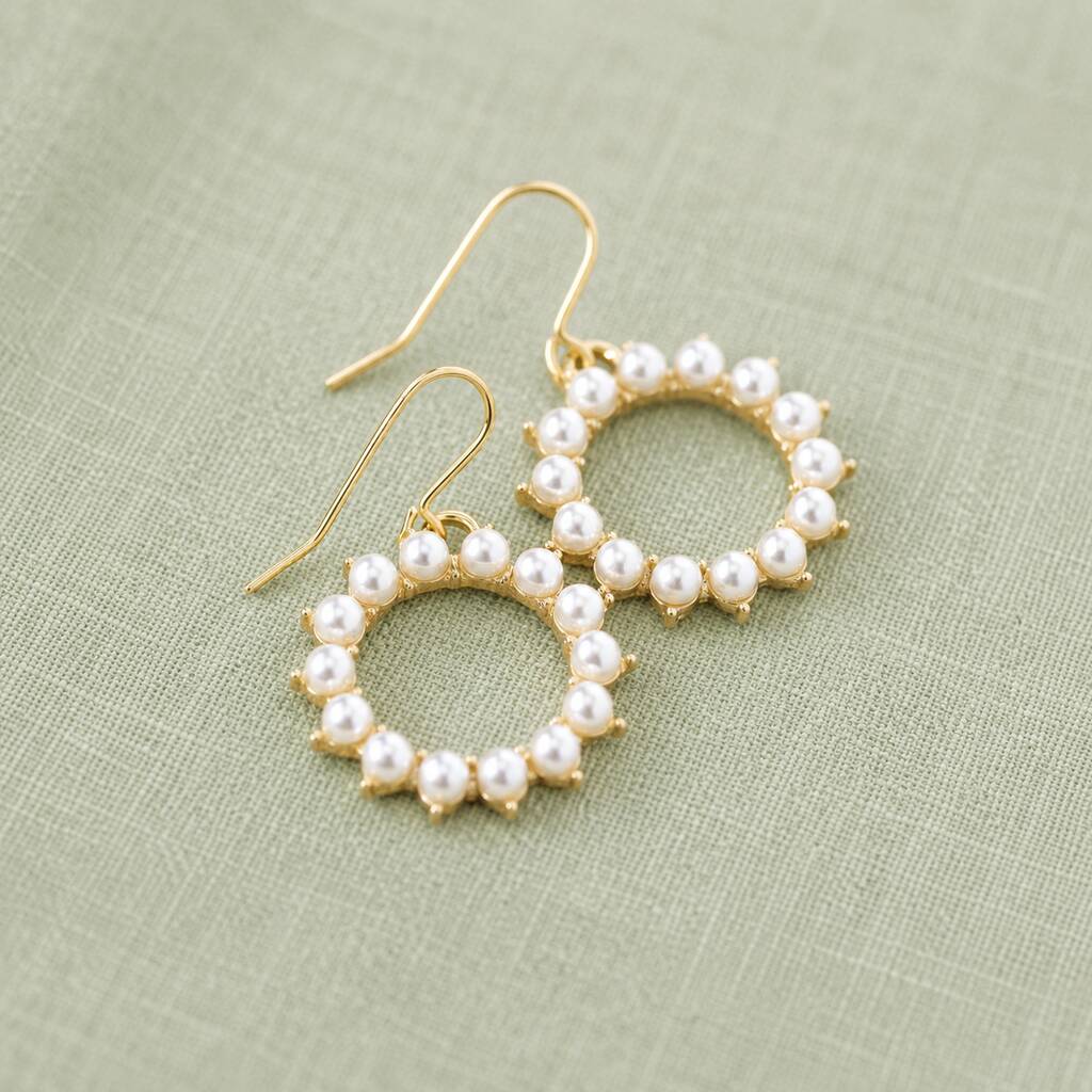 Circular pearl and gold earrings arranged on soft fabric, blending classic pearls with modern design