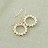 Circular pearl and gold earrings arranged on soft fabric, blending classic pearls with modern design