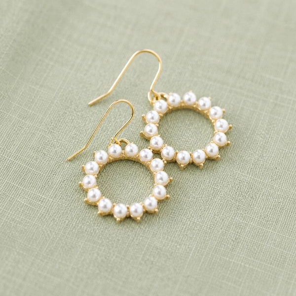 Circular pearl and gold earrings arranged on soft fabric, blending classic pearls with modern design