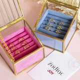 Images shows a selection of gold plated zodiac rings in pink and blue jewellery trinket boxes