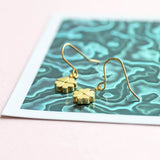 Gold plated four leaf clover earrings displayed on a pink and metallic green background.