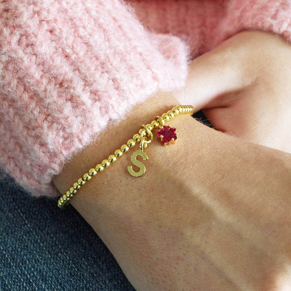 Model wears Gold Plated Initial and Birthstone Star Bracelet with the initial 'S' and July Ruby star birthstone.