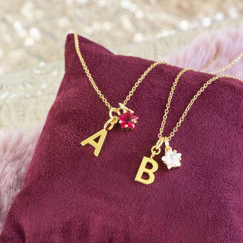 Image shows Gold Plated Initial and Birthstone Star Necklaces from left to right - 'A' with July Ruby and 'B' with April Crystal birthstones.