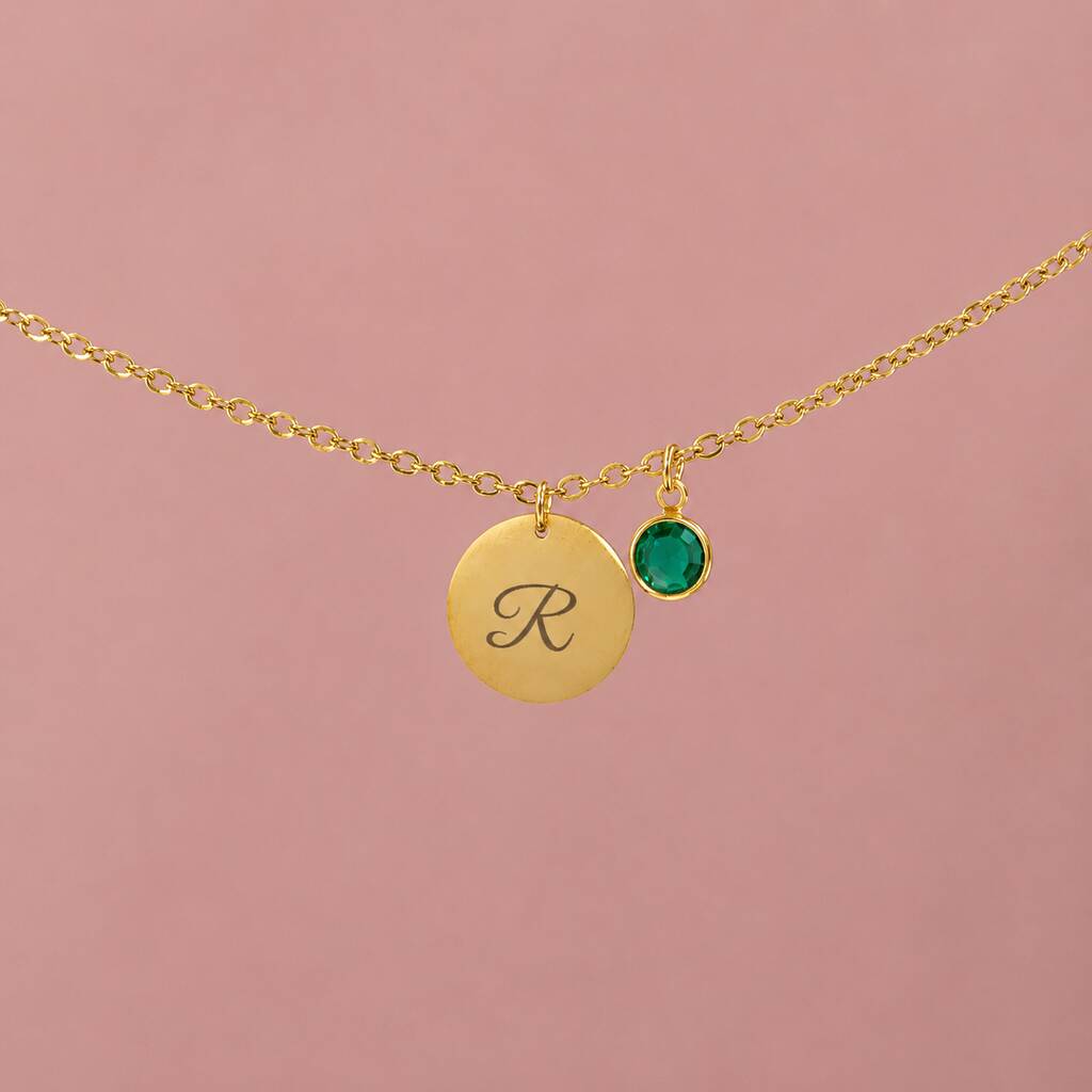 Close-up of gold initial necklace with script R pendant and green birthstone charm on a delicate chain
