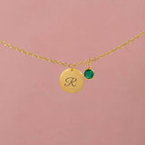 Close-up of gold initial necklace with script R pendant and green birthstone charm on a delicate chain