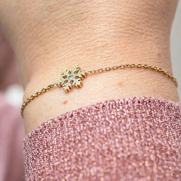 Lady wearing a gold plated snowflake charm necklace adorned with a crystal worn on the wrist with a pink sparkly jumper.