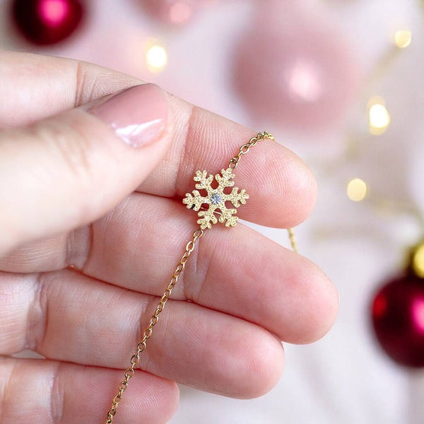 Gold plated sparkly snowflake bracelet presented on a Christmas red and pink bauble background.