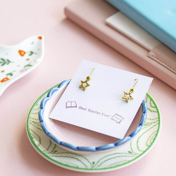 Gold plated cut out star drop earrings displayed on a Best Teacher Ever sentiment card set on top of 2 porcelain floral trinket plates