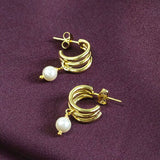 Image shows Gold Plated Triple Hoop Pearl Earrings on a maroon backdrop.