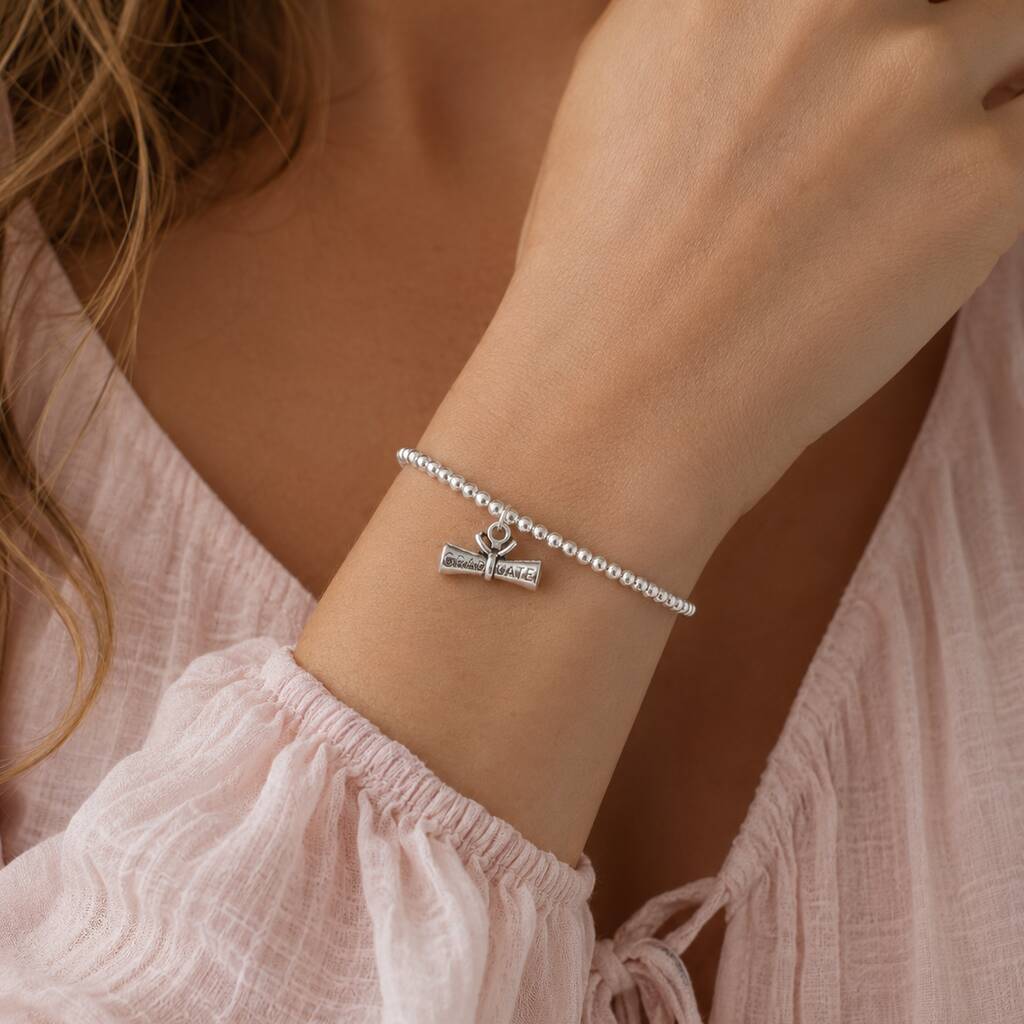 Silver plated graduation charm bracelet with stretch bead band and scroll charm, delicate layered jewellery style.