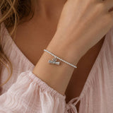 Silver plated graduation charm bracelet with stretch bead band and scroll charm, delicate layered jewellery style.