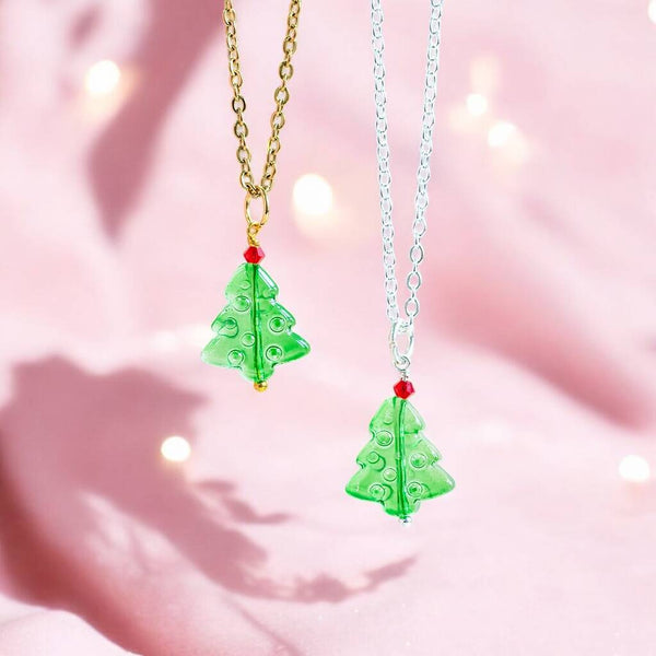 Image shows two green glass Christmas tree pendant necklaces with a red bed bauble at the top of the tree. One pendant is on a silver chain and the other pendant is on a gold chain.