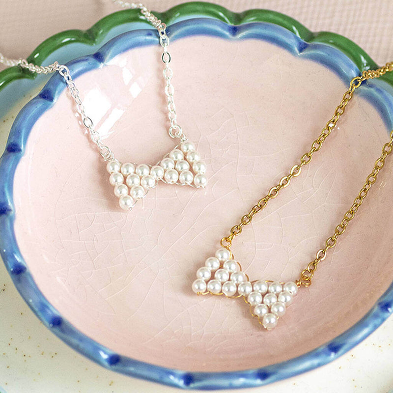 Image shows from left to right: silver plated Hand Beaded Pearl Bow Necklace and gold plated Hand Beaded Pearl Bow Necklace sitting in a pink decorative jewellery holder.