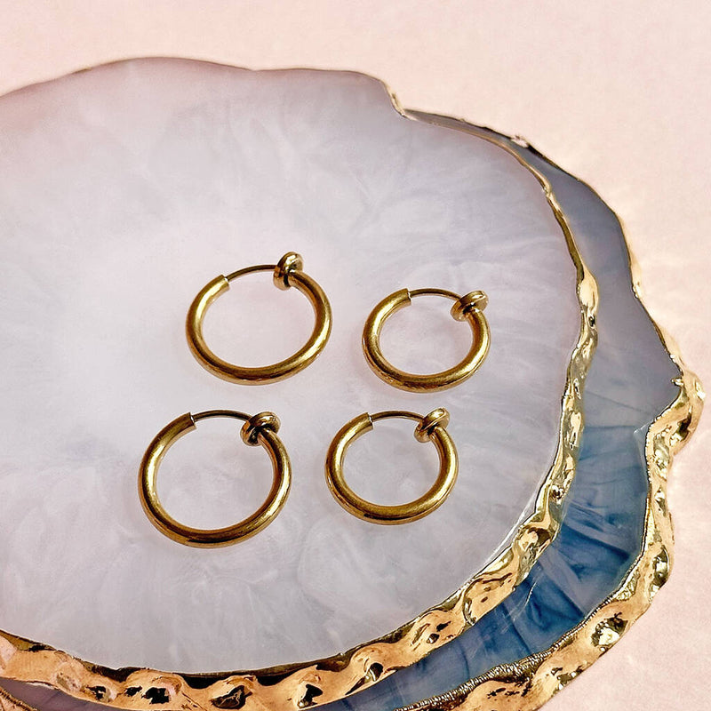 Image shows fake piercing gold hoop earrings on a marble trinket dish