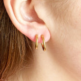 Image shows a model wearing two gold hoop earrings for non pierced ears
