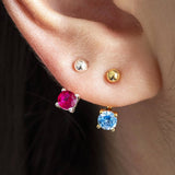 Two pairs of Illusion Birthstone Stud Earrings with a classic round-cut gemstone set in a minimalist prong setting, designed to showcase the birthstone's vibrant colour and clarity. Worn on an earlobe.